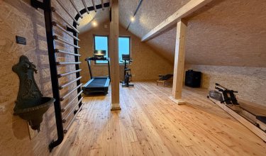 Dachboden-Fitnessraum mit Holzfußboden, Sprossenwand, Laufband, Fahrradtrainer und Rudergerät