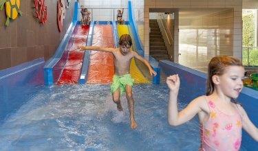 Kinder rutschen auf bunten Wasserrutschen in einem Hallenbad mit flachem Wasser