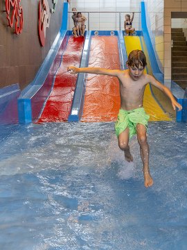 Kinder rutschen auf bunten Wasserrutschen in einem Hallenbad mit flachem Wasser