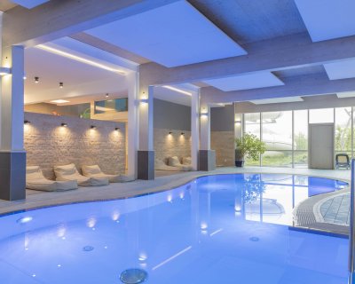 Innenaufnahme eines modernen Hallenbads mit blauer Beleuchtung und Liegestühlen am Rand