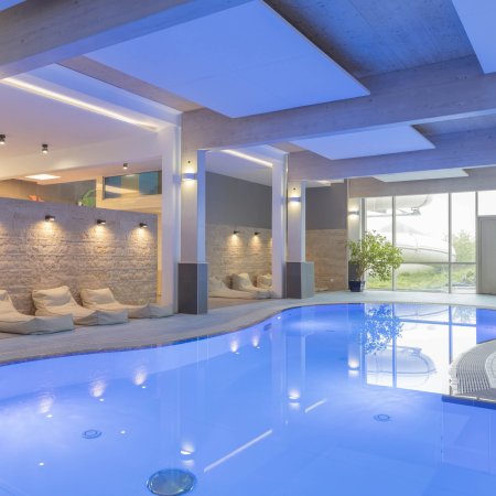 Innenaufnahme eines modernen Hallenbads mit blauer Beleuchtung und Liegestühlen am Rand