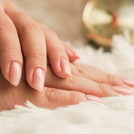 Zwei Hände mit gepflegten, rosa lackierten Nägeln auf weißem flauschigem Untergrund
