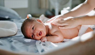 Baby liegt auf dem Bauch auf einer Decke, Hände massieren sanft den Rücken