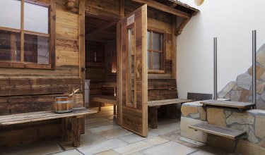Holzsauna mit offener Tür, Holzbänken und einem Holzeimer auf der linken Bank