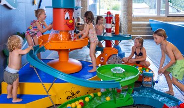 Kinder spielen an einem bunten Wasserspiel mit Rutschen und Bällen in einem Hallenbad