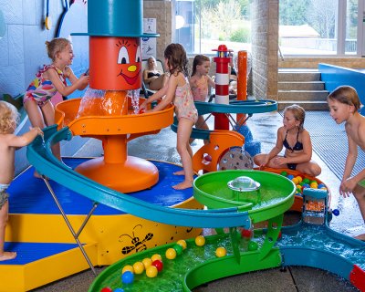 Kinder spielen an einem bunten Wasserspiel mit Rutschen und Bällen in einem Hallenbad