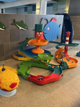 Bunte Spielanlage mit Kugelbahn und Fischmotiven neben einem Hallenbad