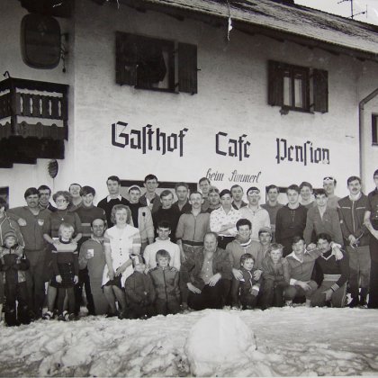 Schwarzweißfoto einer großen Gruppe vor Gasthof Cafe Pension bei Schnee