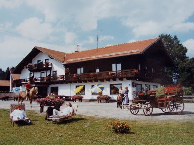 Bauernhaus mit Balkon und Blumendekoration, Menschen entspannen auf Liegestühlen und reiten Pferd vor dem Haus