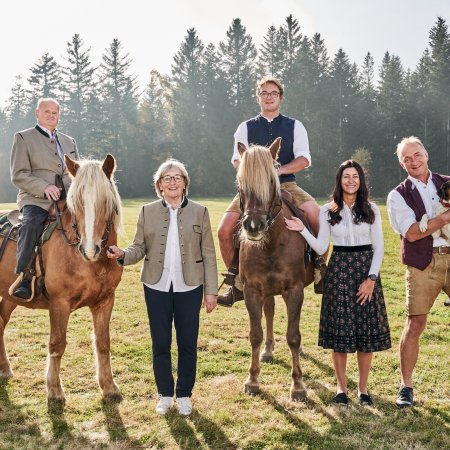 Fünf Personen auf einer Wiese mit zwei Pferden und einem Hund, Wald im Hintergrund