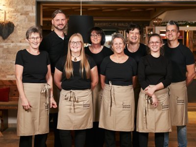 Gruppenfoto von acht Mitarbeitern mit schwarzen Oberteilen und beigen Schürzen im Restaurant