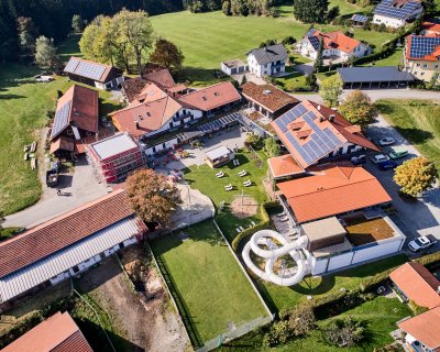 Luftaufnahme eines ländlichen Gebäudekomplexes mit Solarpanelen auf den Dächern und einer großen Wasserrutsche