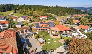 Luftaufnahme eines Dorfes mit Häusern, Solarpaneelen auf Dächern und Spielplatz im Vordergrund