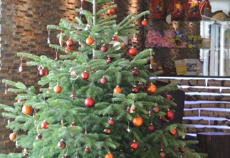 Geschmückter Weihnachtsbaum mit roten und orangen Kugeln in einem modernen Raum mit Steinwand