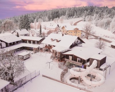 Verschneite Häuser und ein verschneiter Wasserrutschenpark vor einem Wald bei Sonnenuntergang
