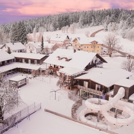 Verschneites Dorf mit Häusern und einer Wasserrutsche vor einem Wald bei Sonnenuntergang
