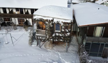 Vogelperspektive auf schneebedecktes Baumhaus neben Wohngebäuden mit Schaukel im Vordergrund