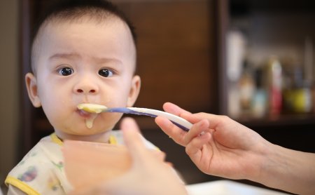 Nahaufnahme eines Babys, das mit einem Löffel Brei gefüttert wird, Hand hält Löffel und Schüssel