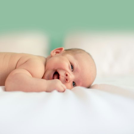 Lächendes Baby liegt auf dem Bauch auf weißem Bett vor grünem Hintergrund