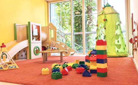 Bunter Spielraum mit Rutsche, Bauklötzen, grünem Zelt und großen Fenstern