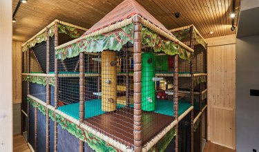 Innenansicht eines mehrstöckigen, netzumsponnenen Klettergerüsts mit Holzdecke und Holzwänden