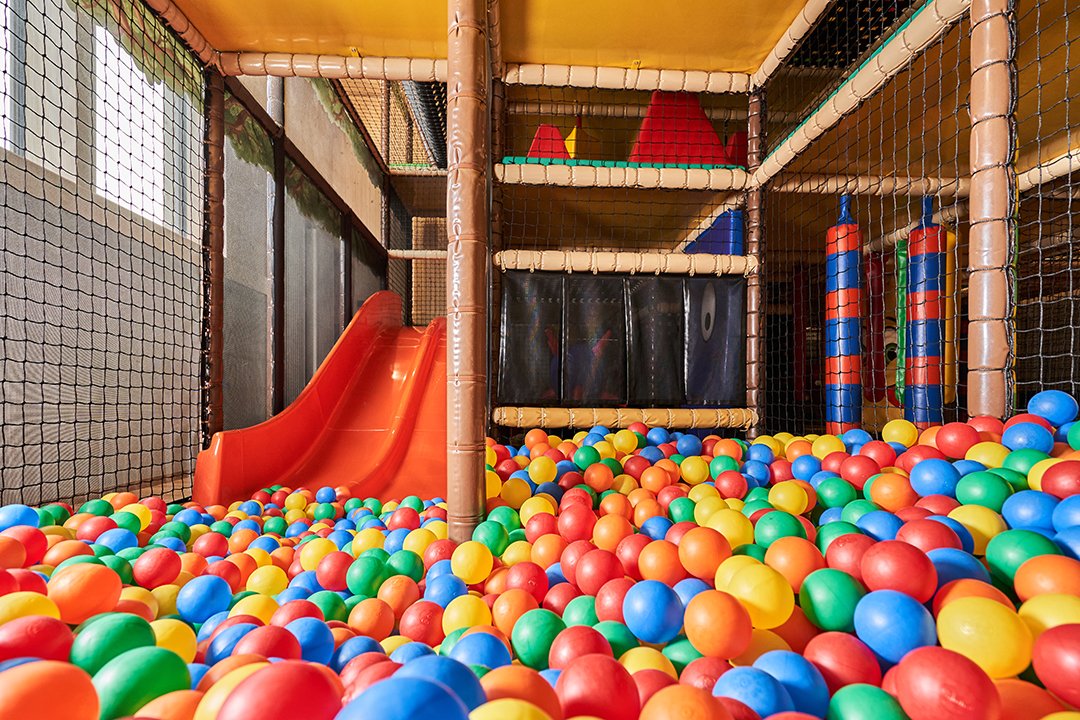 Bunter Bällepool mit roter Rutsche und Klettergerüst in einem Indoor-Spielplatz