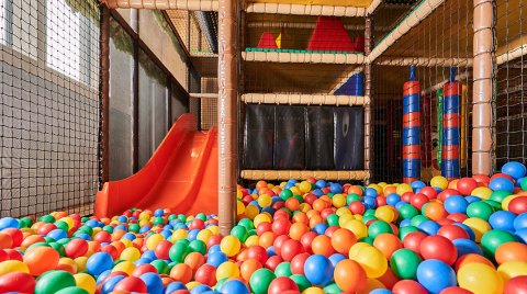 Bunter Bällepool mit roter Rutsche und Klettergerüst in einem Indoor-Spielplatz