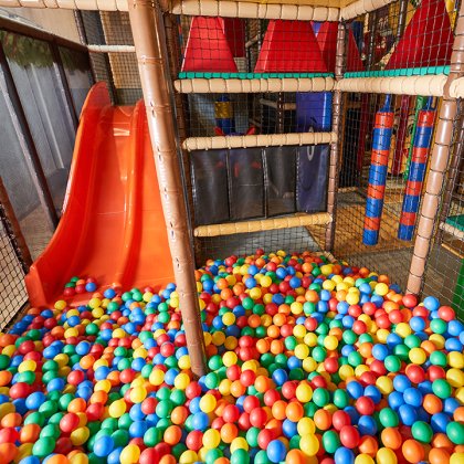 Blick auf eine bunte Bällebadfläche mit einer orangen Rutsche und Klettergerüst im Innen-Spielplatz