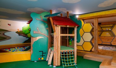 Bunter Indoor-Spielplatz mit Holzhaus, Kletternetz, Bällebad und Wabenregalen an der Wand