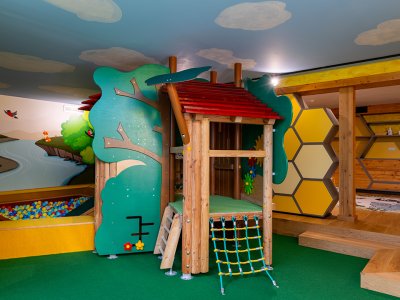 Bunter Indoor-Spielplatz mit Holzhaus, Kletternetz, Bällebad und Wabenregalen an der Wand