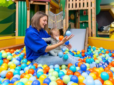 Frau und Baby sitzen im Bällebad eines Spielplatzes, umgeben von bunten Bällen