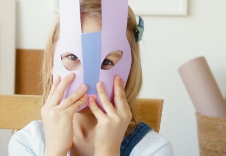 Kind sitzt am Tisch und hält eine selbstgebastelte Hasenmaske vor das Gesicht