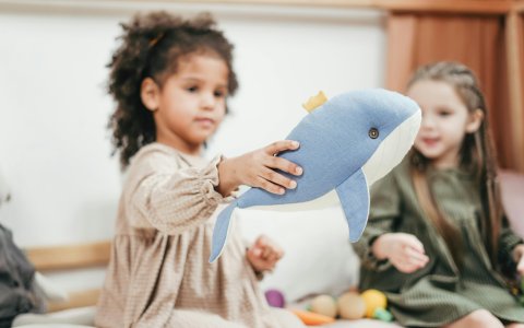 Kind hält ein blaues Stofftier in Form eines Wals, andere Kinder sitzen im Hintergrund