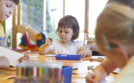 Kinder sitzen an einem Tisch und malen mit Buntstiften in einem hellen Raum