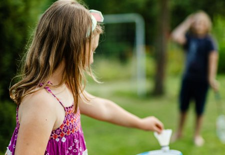 Mädchen im bunten Kleid spielt Badminton im Garten, Junge im Hintergrund unscharf