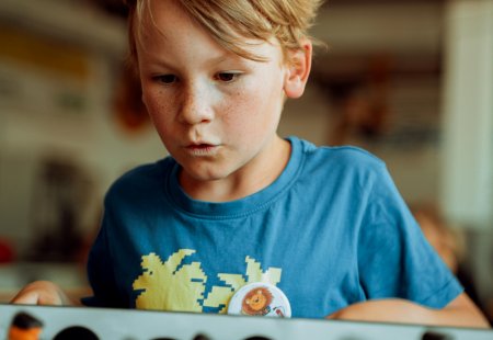 Junge mit Sommersprossen und blauem T-Shirt spielt Tischfußball in Innenraum