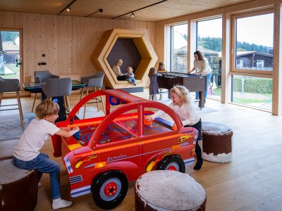 Kinder spielen an einem roten Auto-Airhockey-Tisch in einem hellen Holzraum mit großen Fenstern