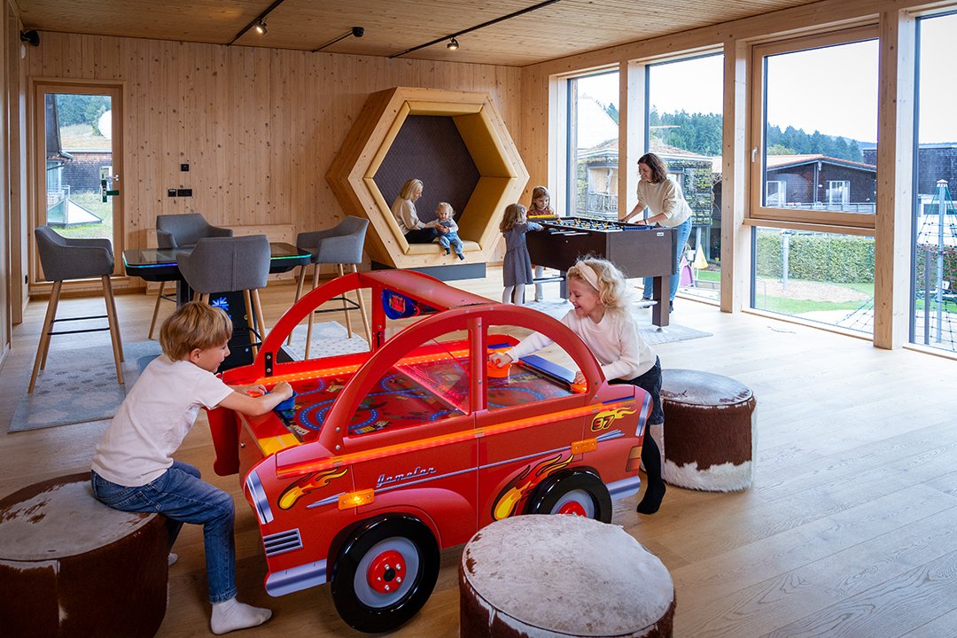 Kinder spielen an einem roten Auto-Airhockey-Tisch in einem hellen Holzraum mit großen Fenstern