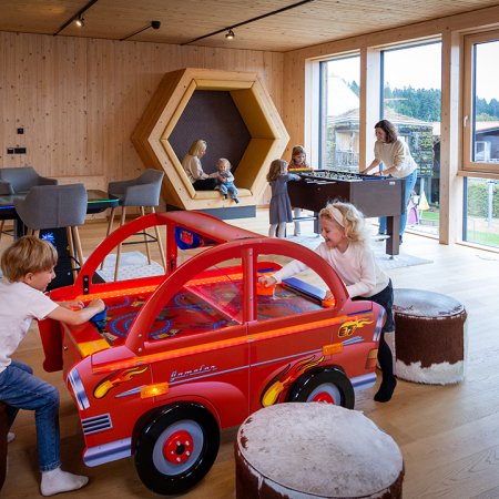 Kinder spielen an einem roten Auto-Airhockey-Tisch in einem hellen Holzraum mit großen Fenstern