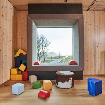 Holzraum mit großem quadratischem Fenster, bunten Sitzwürfeln und einem Pac-Man-Spielautomat
