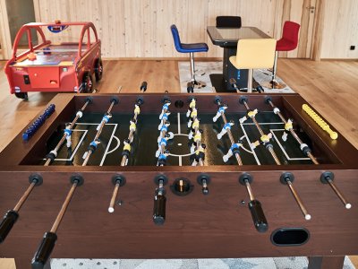 Tischfußballspiel in einem Raum mit bunten Stühlen und einem roten Spieltisch im Hintergrund