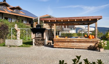 Holzüberdachte Außenküche mit Kürbissen und Holzofen neben einem Haus mit Solarpaneelen