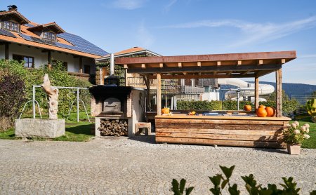 Holzüberdachte Außenküche mit Kürbissen und Holzofen neben einem Haus mit Solarpaneelen