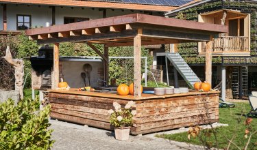 Holzüberdachte Außenküche mit Kürbissen und Tellern vor einem Haus mit Solarpaneelen