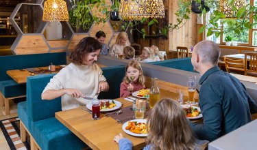 Familie mit Kindern isst in einem gemütlichen Restaurant mit Holzwänden und Pflanzen