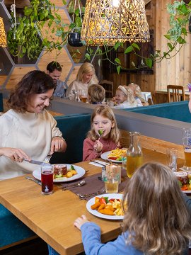 Familie mit Kindern isst in einem gemütlichen Restaurant mit Holzwänden und Pflanzen