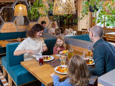 Familie mit Kindern isst in einem gemütlichen Restaurant mit Holzwänden und Pflanzen