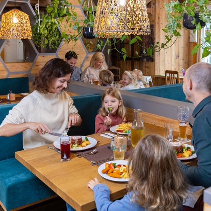 Familie mit Kindern isst in einem gemütlichen Restaurant mit Holzwänden und Pflanzen