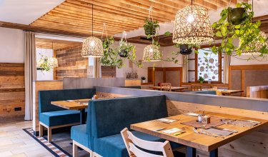 Gemütliches Restaurant mit Holzmöbeln, blauen Sitzbänken, hängenden Pflanzen und geflochtenen Lampen
