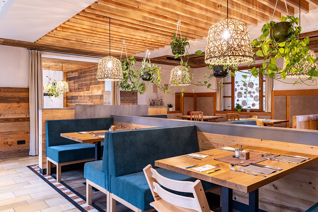 Gemütliches Restaurant mit Holzmöbeln, blauen Sitzbänken, hängenden Pflanzen und geflochtenen Lampen